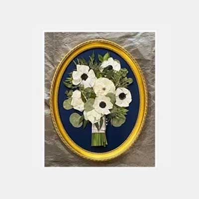 White anemone flower bouquet in a gold oval frame on a blue background.