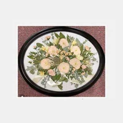 Oval framed floral arrangement with pink and yellow flowers and greenery.