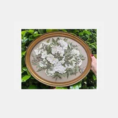 Oval framed embroidery of white flowers and green leaves.