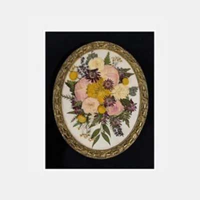 Oval pressed flower arrangement in ornate gold frame, set on black background.