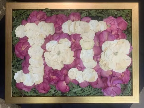 "Pink and white floral arrangement in a gold frame, spelling out the name "Toto" with white petals."