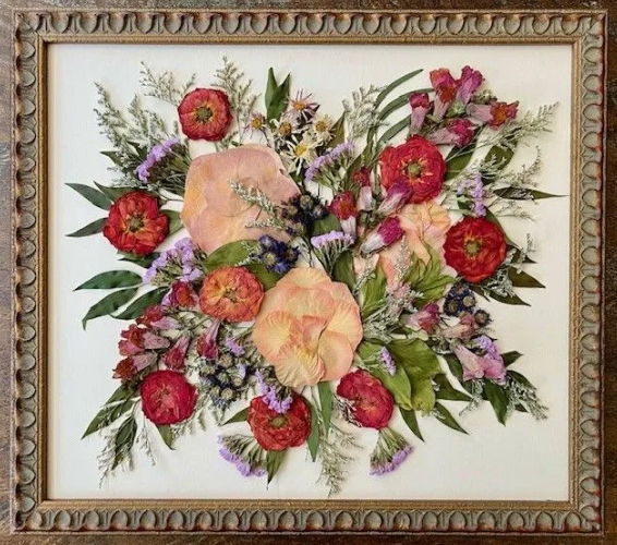 Pressed flower arrangement in a gold frame, featuring red, pink, purple, and green dried flowers.