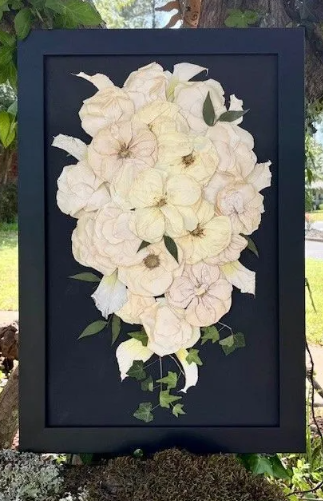Framed pressed flower bouquet in shades of white and green on a dark background.