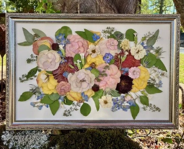 Framed dried flower arrangement: pink, yellow, and blue blooms with green leaves.