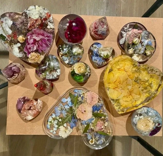 Various resin art pieces with flowers encased in them. Mostly heart-shaped, with blues, pinks, and yellows.
