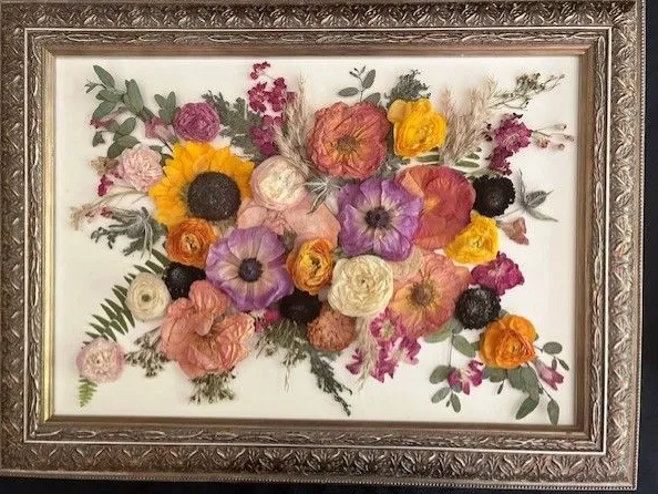Dried flowers art, framed.  Sunflowers, ranunculus, and other colorful flowers arranged on a white background.