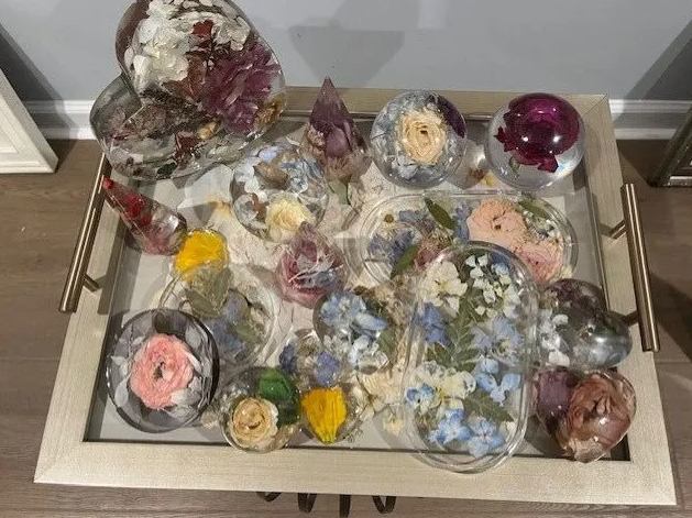 A silver tray holds numerous clear resin art pieces with dried flowers of various colors embedded inside.