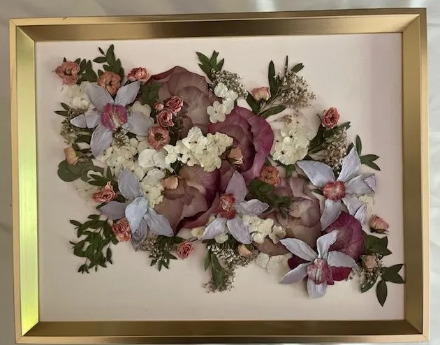 Framed artwork: dried flowers arranged in a floral design, with shades of pink, purple, and green on a cream background.