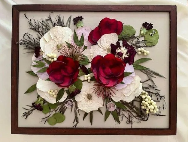 Framed pressed flowers: white and maroon blooms, green leaves, set against light background.