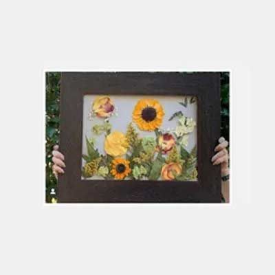 Hands holding framed pressed flowers, sunflowers, and greenery.
