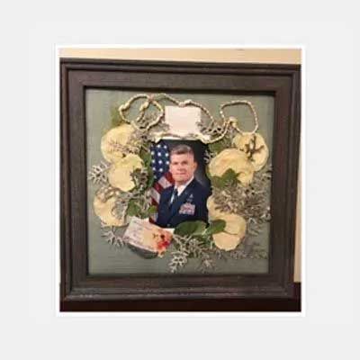 Framed photo with a man in military uniform, surrounded by a wreath with dried flowers, and the American flag.