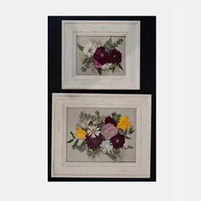 Two framed pressed flower arrangements with white frames on a black background.