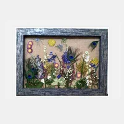 Floral arrangement in a distressed gray frame, including flowers, peacock feathers, and a yellow circle on a tan backdrop.