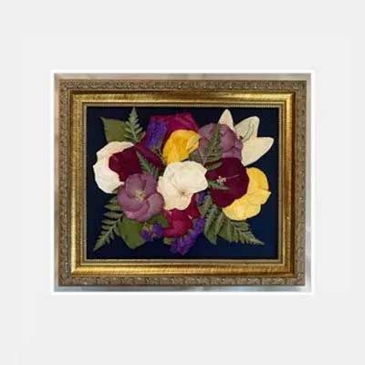 Framed pressed flower bouquet with gold frame on dark blue background, colorful flowers.