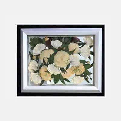 Framed pressed flower arrangement with white and yellow blooms and green leaves.