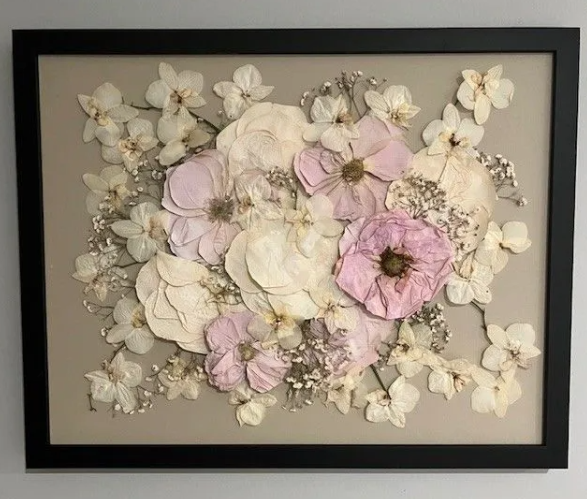 Framed pressed flowers: pink, cream, and white blooms on a neutral background, in a black frame.
