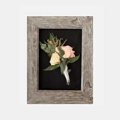 Boutonniere with roses in a weathered grey wooden frame, set against a black backdrop.