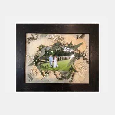 Black framed photo of a couple walking in a field with green foliage framing the image.