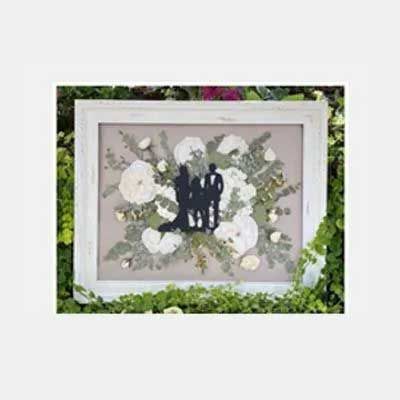 Framed silhouette of a family among dried white flowers, green leaves, and a rustic wooden frame.