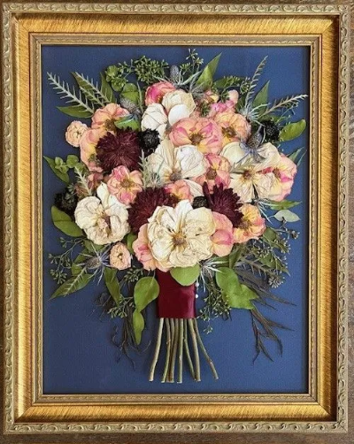 Framed dried flower bouquet; pink, cream, and burgundy blooms with green leaves on a blue background.
