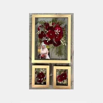 Three gold-framed floral arrangements. One large frame has a photo of a person. All frames feature red flowers.