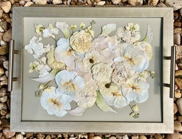 Tray with dried white and yellow flowers, gray background, silver frame.