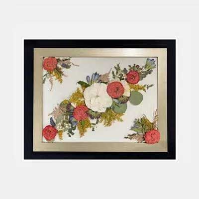 Framed floral arrangement featuring white, red, and green pressed flowers on a light background.