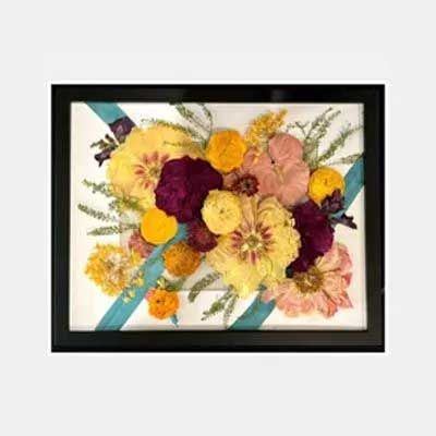 Framed pressed flower arrangement with yellow, pink, and purple flowers on a white and blue background.