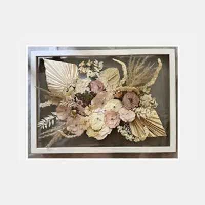 Floral arrangement in a glass frame, with dried flowers in beige, pink, and green.