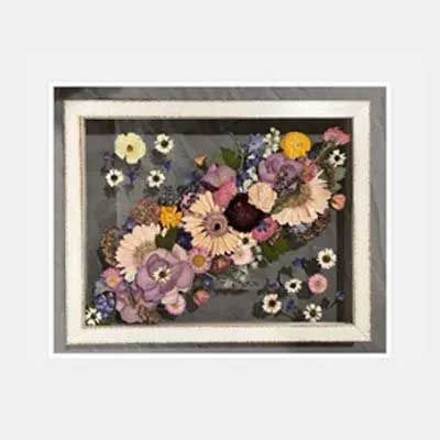 Framed floral arrangement featuring dried flowers in shades of pink, purple, yellow, and white on a gray background.