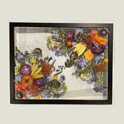 Floral arrangement in black framed shadow box: colorful pressed flowers on white fabric.
