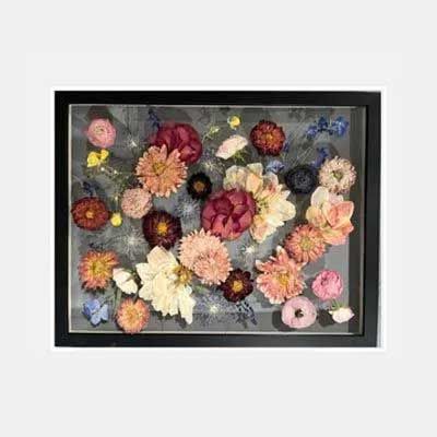 Framed artwork: assorted dried flowers in a shadow box, with a black frame on a gray background.