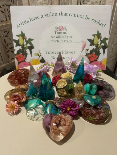 Assorted colorful resin flower bouquets and crystals on a table, with a sign reading "Artists have a vision."