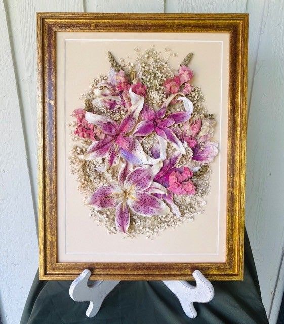 Framed pink and purple floral artwork on a white stand against a pale wall.