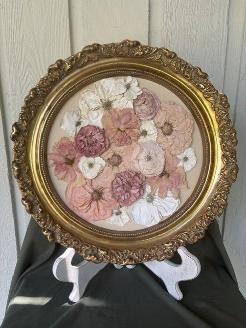 Round gold-framed floral embroidery art on a white stand against a paneled wall.