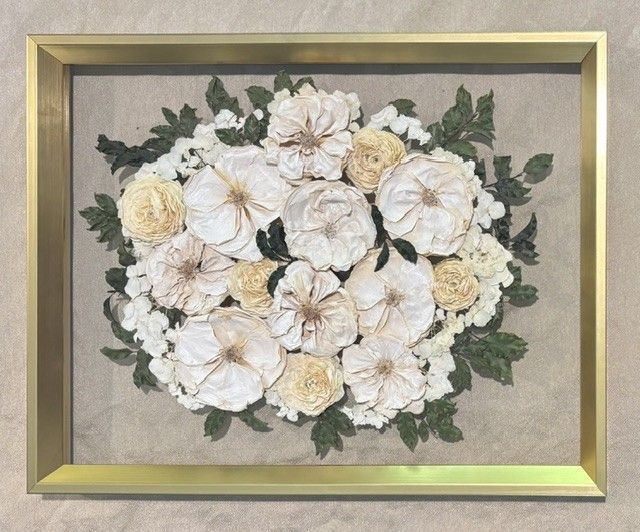 Framed floral arrangement of white and cream flowers with green leaves on a beige background.