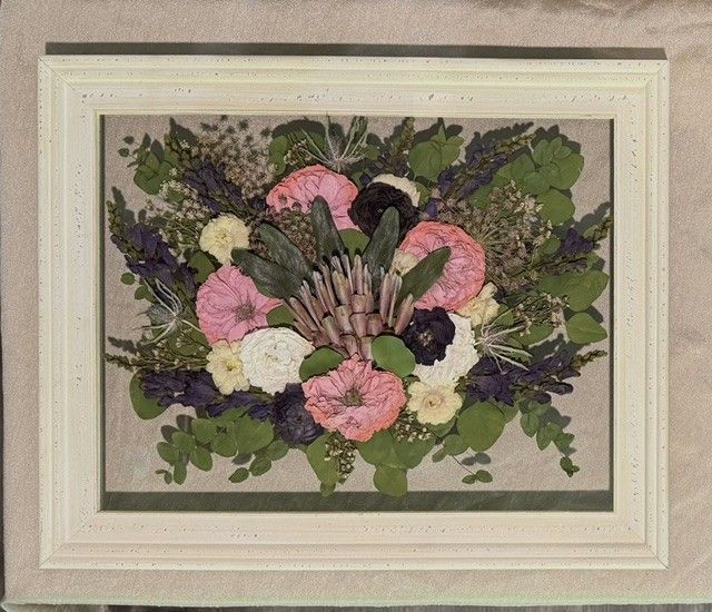 Framed floral arrangement with pink, white, and purple flowers on a beige background.