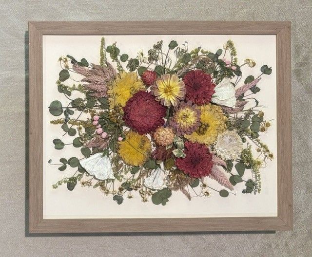 Pressed flower bouquet in a wooden frame with red, yellow, and white blossoms on a cream background.