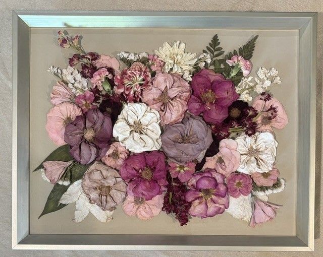 Framed collage of pressed flowers in pink, purple, white, and mauve tones on a neutral background.