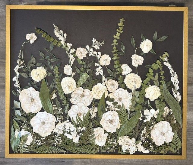 Framed floral artwork with white flowers and green foliage on a dark background.
