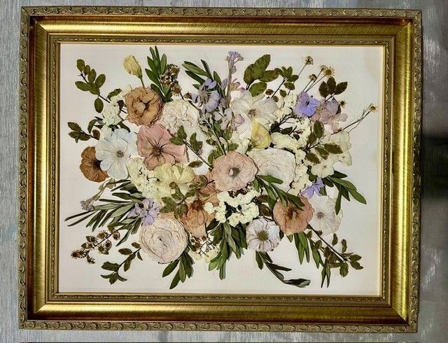 Framed pressed-flower bouquet artwork with pale pink, white, and purple blossoms on a cream background.