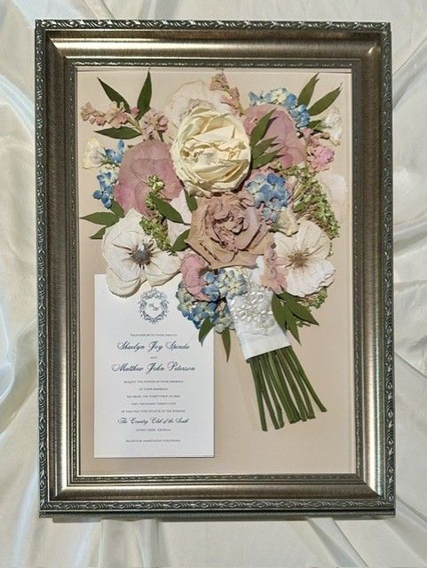 Framed wedding bouquet display with pastel flowers and a small commemorative plaque.