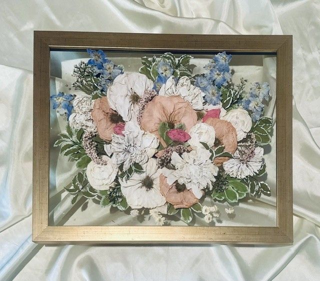 Framed pastel flower bouquet with white, pink, and blue blossoms and green leaves.
