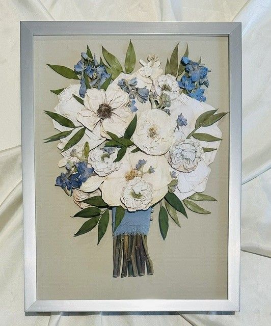 Framed floral bouquet artwork with white and blue flowers and green leaves on a beige background.