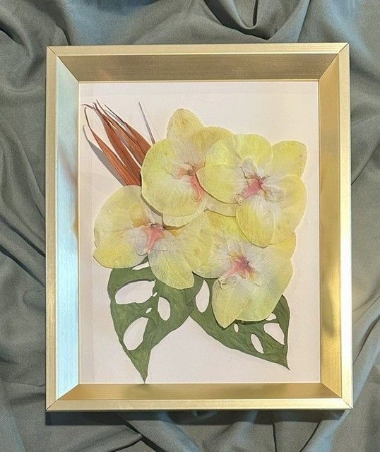 Framed floral artwork with yellow blossoms and green leaves on a blue fabric background.