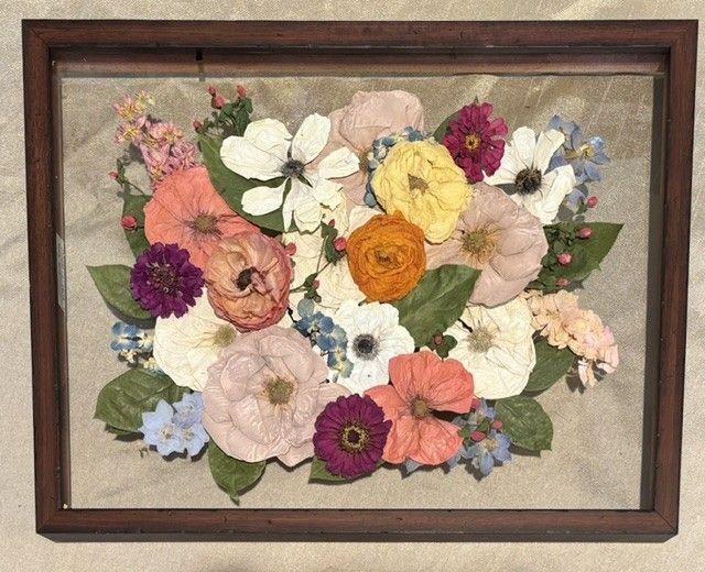 Framed pressed-flower artwork with colorful blooms on a beige background.