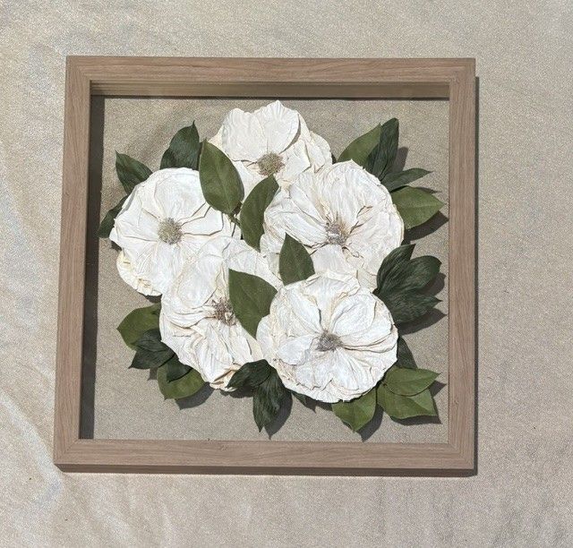 Framed white flower wall art with green leaves on a beige background.