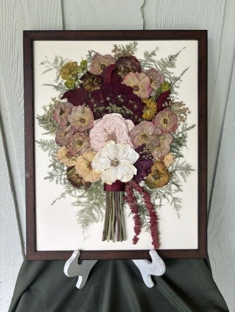 Framed dried floral bouquet with burgundy, pink, and cream flowers on a stand.