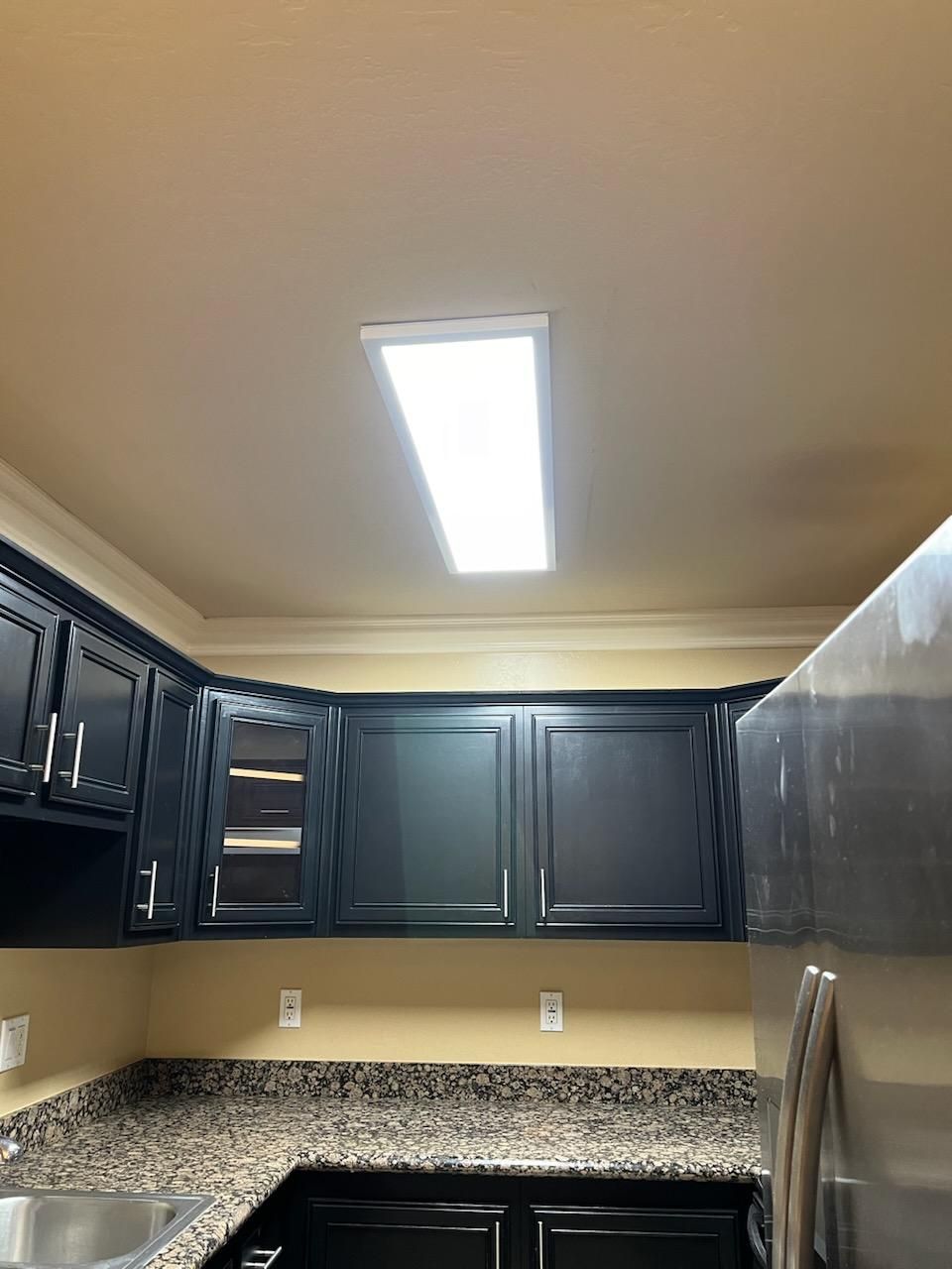 A kitchen with black cabinets , granite counter tops , and a stainless steel refrigerator.