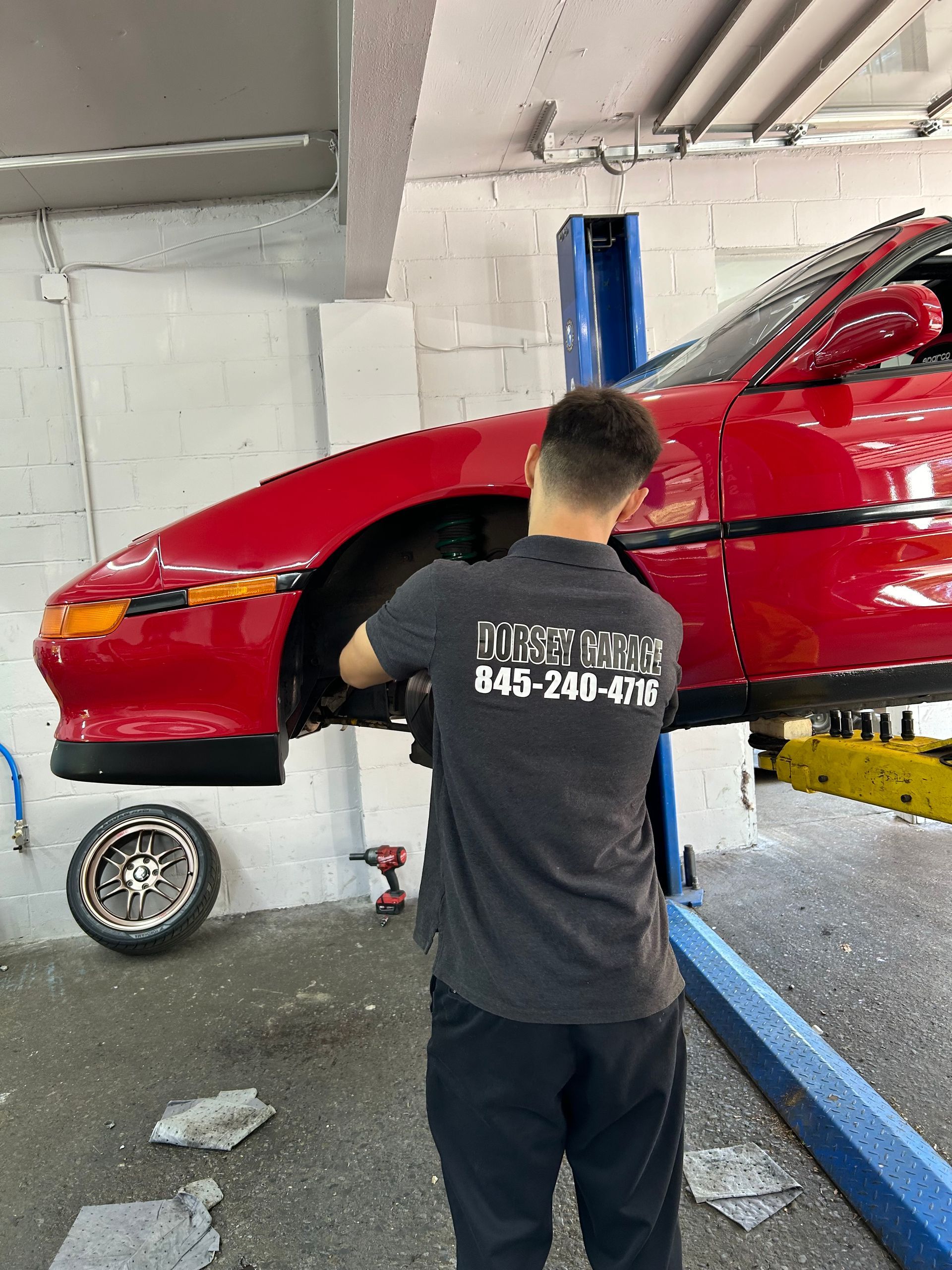 A man is working on a red car on a lift.